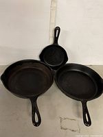 Front view showing three cast iron skillets placed side by side with handles extended outward, showing tops and interiors.