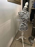Front angled view of one zebra print cloth mannequin on white wooden tripod stand