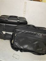 Two black leather briefcases placed on floor, one upright and one lying flat, showing overall size and style.