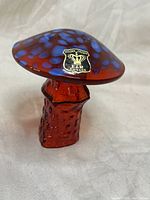 Front angle showing amber-red textured glass stem and blue spotted red cap with Golden Crown E&R Sweden label.