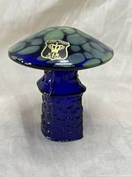 Front view of hand blown art glass mushroom with Golden Crown label on cap, blue and green spotted pattern.