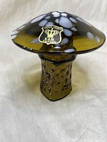 Side view of hand blown glass mushroom with brown translucent base and white spots on dome, featuring original Golden Crown E and R label.