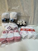 Photo shows multiple packs of new white sport socks with blue and red labels, and some white ankle socks with pink accents, all packaged and stacked.