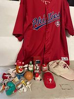 Full lot photo showing red Phillies jersey and various Phillies collectibles including Mr. Potato Head figure, hats, mug, and loose parts.