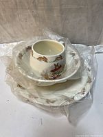 Photo of the plate, bowl, and handled mug wrapped in clear plastic showing the full set stacked together.