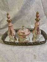 Porcelain pink Limoges perfume bottles and matching powder jar displayed on mirrored brass dresser tray.