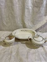 View of the serving bowl, cream pitcher, and sugar bowl with lid arranged on white fabric backdrop.
