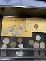 Photo showing Canadian 5 cent coins from 1968 to 1975, Littleton Stamp & Coin Co. envelope with Hungary bronze 2 Fillér coin from 1958, plus assorted other coins.