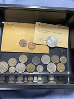 Top view of coins laid out in black tray showing two coins in labeled envelope 'Bahamas 1 Cent' and the South Vietnam coin with a Littleton label