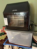 Front view of black PowerAirFryer Oven Elite air fryer sitting on a clear plastic storage bin containing accessories.