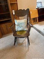 Full frontal view of the antique wooden rocking chair showing fabric cushion seat and armrests.