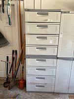 Two stacked Black & Decker plastic storage cabinets with 4 drawers each, showing overall front view, stored in a garage with tools beside them.