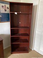 Front view of the tall wooden bookcase showing five shelves and cable management holes.