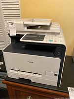 Front-right angle photo showing the Canon multifunction printer with scanner lid, control panel and brand logo.