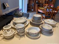 Full view of the dish set showing multiple stacks of plates, bowls, serving pieces including covered sugar bowl and gravy boat, with visible gold and floral decoration.