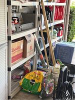 Four bags of garden soil and fertilizer, plus a roll of landscaping fabric and garden tools leaning against shelves.