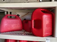 Three red plastic gasoline containers on a plastic shelf, showing brand names and capacity markings.