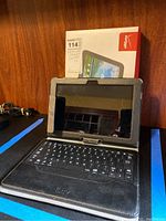 Front view of iLuv tablet in black leather case with attached keyboard, set upright with Verizon box behind