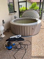 Full view of inflated hot tub with pump and cords on patio beside wall