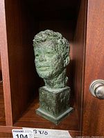 Front view of bronze JFK bust in cubby shelf, showing textural detail and facial features.