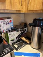 Digital kitchen scale with clear cover on box next to mandoline cutting board and coffee thermos dispenser.