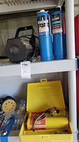 Four propane canisters (two blue, two yellow), two nozzles, and a propane torch placed on shelving.