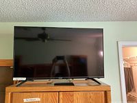 Front view of Sharp 40-inch flat screen TV placed on wooden cabinet with remote resting on cabinet.