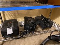 Three black surge protectors placed side by side on a metal shelf, showing cords and outlets.