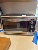 Front view of Oster toaster oven on kitchen counter, showing glass door and stainless steel body.