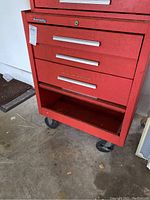 Front view showing three drawers with silver handles, Kennedy brand badge, and open bottom shelf with caster wheels underneath.