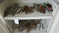 Miscellaneous worn hand tools including locking pliers, adjustable wrenches, and various screwdrivers on two white shelves.