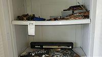 Two shelves filled with various hand tools including an Allen socket set in black case and other metal tools scattered around.