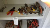 Two shelves filled with various hand tools including pliers, knives, screwdrivers, wire cutters, and scissors; visible wear and dirt on tools.