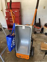 Front view of the Worx convertible wheelbarrow showing the orange handles with black grips, gray tub, and large black and orange tires.