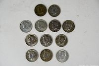 12 Kennedy half dollar coins laid out individually showing obverse side with Kennedy's profile and dates 1965-1969 in varying conditions.