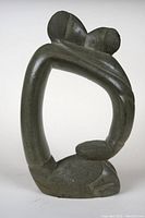 Photo front angle of abstract stone sculpture depicting two people with arms around each other forming an open loop shape.