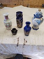 All five Asian ceramic items on a cloth-covered surface: three vases, one teapot, one covered jar.