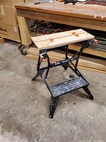 Black & Decker Workmate 200 standing open with wooden top showing paint splatters and orange clamps on work surface.