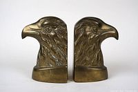 Pair of brass bookends shaped like detailed eagle heads, side by side, showing front and profile views.