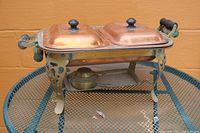 Full view of copper serving tray with two covered compartments and metal frame with wooden handles