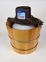 Photo of Rival electric ice cream maker on wooden bucket showing front and top with sticker and cord.