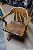 View of the wooden desk chair showing the contoured seat, vertical slatted backrest, and curved armrests.