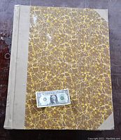 Full top view of large bound book with marbled cover and a US dollar bill for scale.