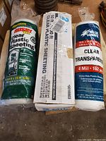 Photo of three rolls of clear plastic sheeting from different brands, with labels visible showing size and thickness.