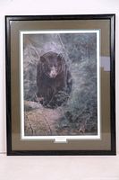 Framed print showing full art of a black bear in a woodland scene, surrounded by pine and branches in green and brown tones.