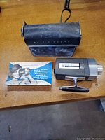 Bell & Howell Super 8 camera with carrying case and instruction manual shown on wooden surface.