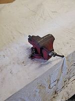 Front perspective of vintage red metal bench vise with closed jaws and swivel base on white cloth.