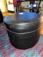 Close-up side angle showing black round faux leather upholstered footstool with some surface wear.