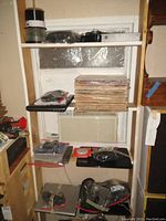 Photo of shelving unit with stacks of vinyl records and several laptops and electronic devices on shelves