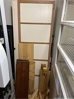 Photo showing white framed folding door leaning against a wall with assorted scrap wood pieces piled in front and beside it.